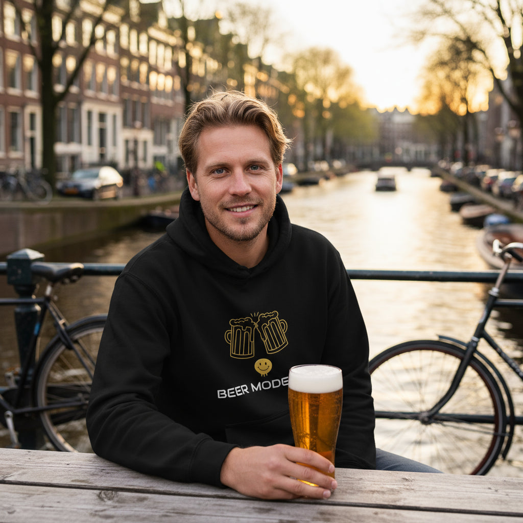 Beer Mode On premium black hoodie lifestyle photo Amsterdam canal beer garden Netherlands - Dutch man early 30s blonde hair outdoor picnic table canal houses bicycles Dutch pilsner golden hour - bold white text graphic craft beer enthusiast European beer culture Amsterdam lifestyle Dutch fashion canal city unisex hoodie Guapo Originals Premium Designer Collection €39.99 Spain